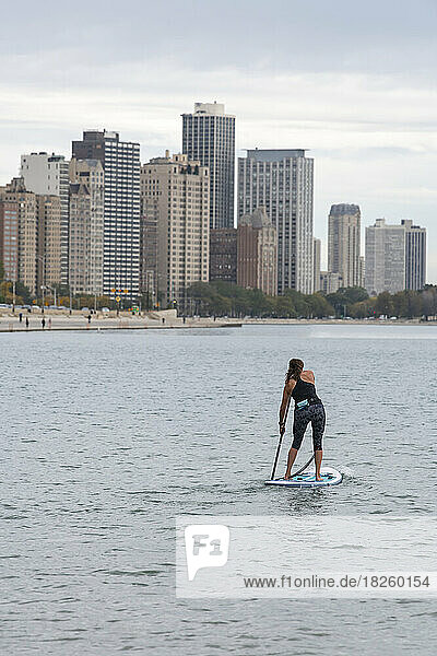 Rear view of woman paddleboarding in lake with city in background