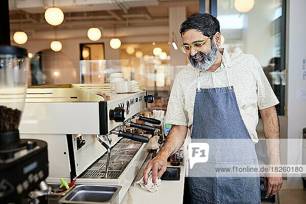 Smiling mature male entrepreneur cleaning kitchen counter in cafe