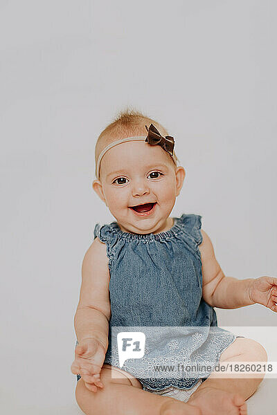 Smiling  happy baby girl in jean dress and a bow on her head