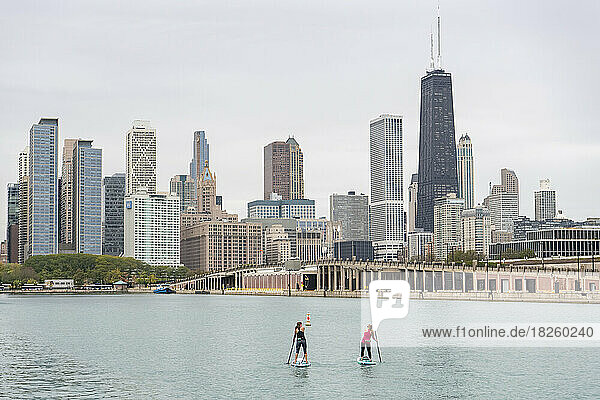 friends paddleboarding together in lake with city in background