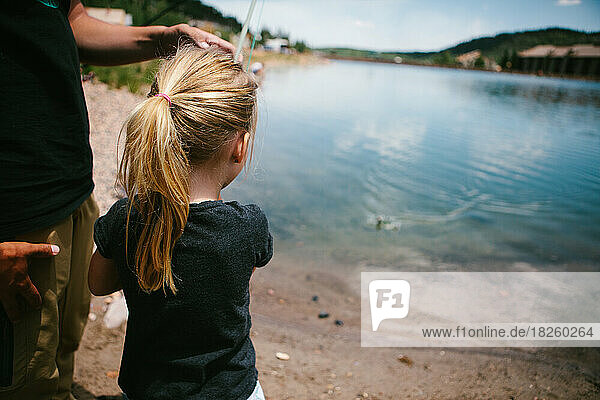 Girl fishes with a fishing pole at a mountain pond on vacation