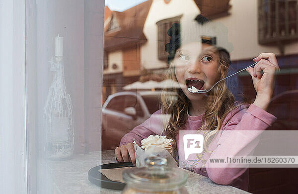 girl drinking hot chocolate and eating cake in a cafe window seat