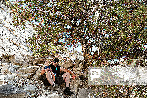Dad and child resting under shade tree on hike