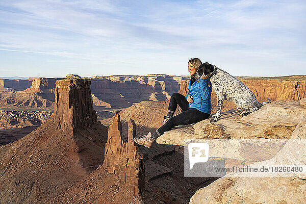 Happy woman looking at view while sitting with dog on rock in desert