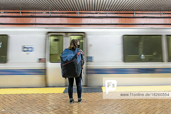 Rear view of woman carrying bag standing in front of subway train