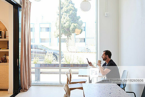 Mature man using mobile phone while having coffee in cafe