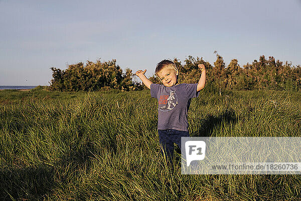 A young boy smiling in a grass meadow on the coast