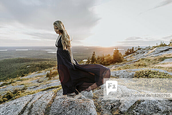 wind blows woman with long hair and dress at sunset on mountain