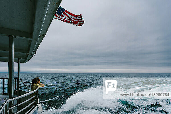 Girl overlooks ocean or lake on back of boat with American flag