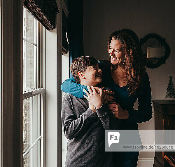Happy mother and son embracing beside a window at home.