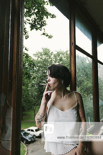 Woman with tattoos smoking while standing on the balcony