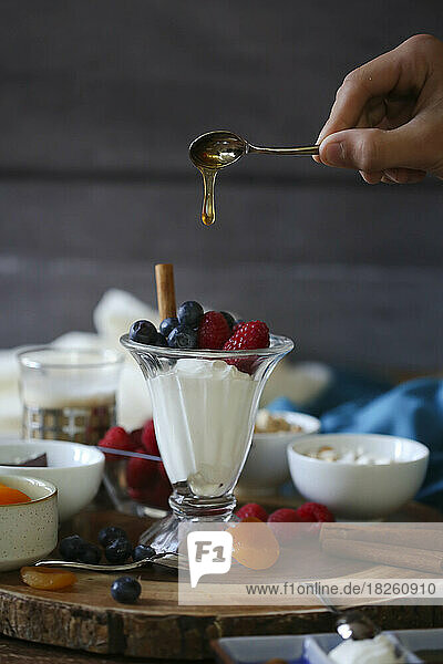 honey dripping from spoon onto fruit and yogurt parfait
