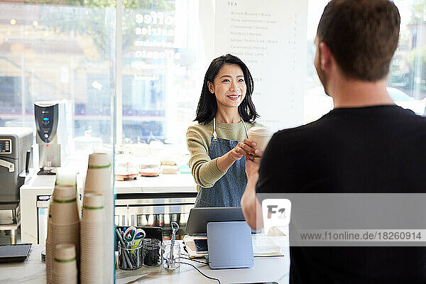 Smiling female saleswoman giving coffee cup to male customer in cafe