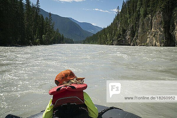 A child in life jacket sits on the bow of a raft in a wide river