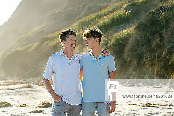 Father And Teenaged Son Smile At Each Other At The Beach