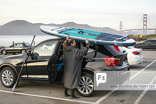 woman unloading paddleboard from car roof at parking lot