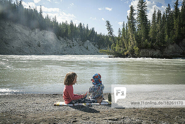 Two children sit on a river beach