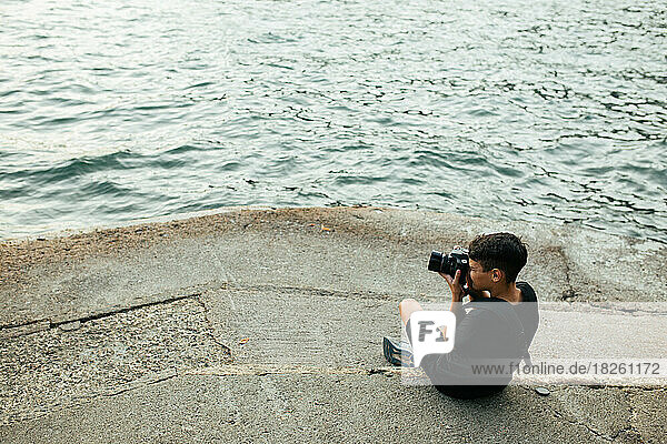 Boy Sits By Lake Como And Photographs The Scene