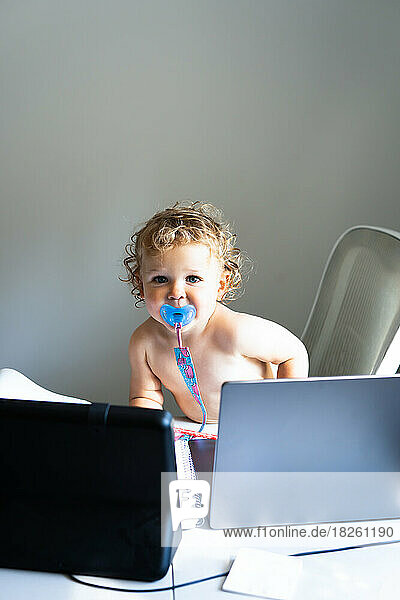 Cute baby boy with pacifier and laptop on the table