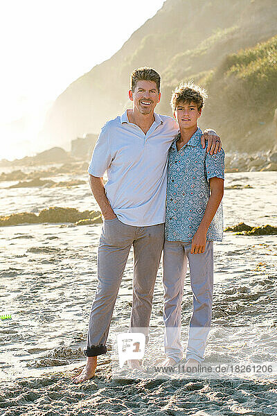 Father And Teen Son Smile For A Photo At The Beach