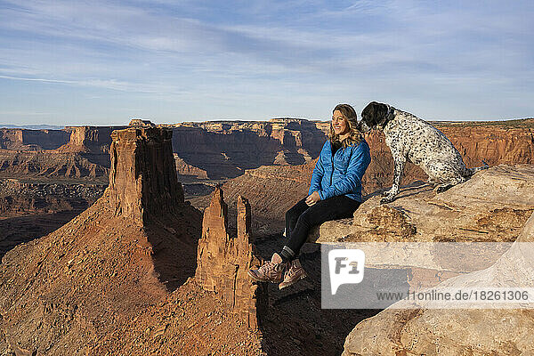 Happy woman looking at view while sitting by dog on edge in desert