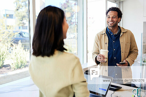 Smiling male customer with coffee cup talking to owner in cafe