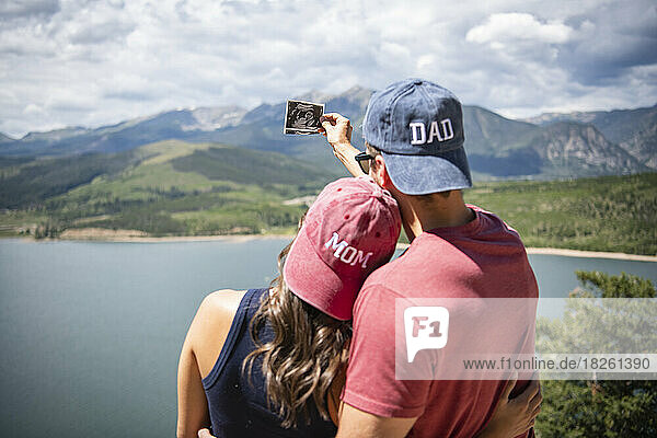 Rear view of couple wearing mom and dad caps holding ultrasound