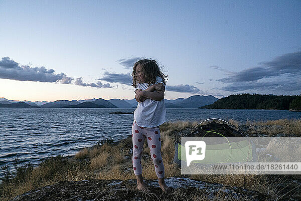 A young girl camping on a grassy island at dusk