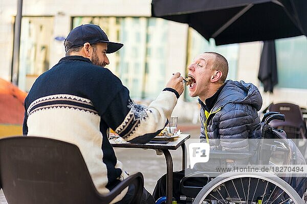 Eine behinderte Person isst mit Hilfe eines Bruders und hat Spaß  Terrasse eines Restaurants
