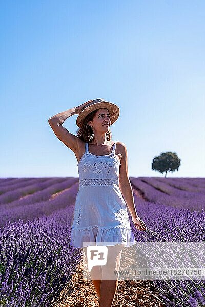 Lebensstil einer lächelnden Frau in einem sommerlichen Lavendelfeld  die ein weißes Kleid und einen Hut trägt