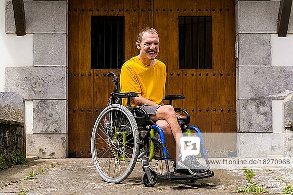 Portrait of a disabled person dressed in yellow in a wheelchair in the entrance of his house smiling