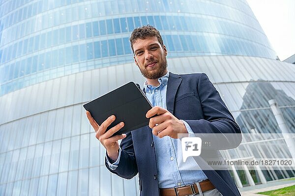 Porträt eines männlichen Geschäftsmannes oder Unternehmers außerhalb des Büros  der ein Tablet in einem Glasgebäude benutzt