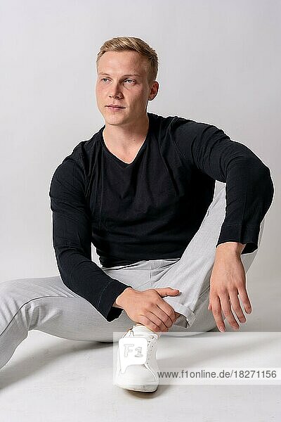 Kaukasisches blondes Modell in einem schwarzen Pullover auf weißem Hintergrund  auf dem Boden sitzend mit verführerischem Blick