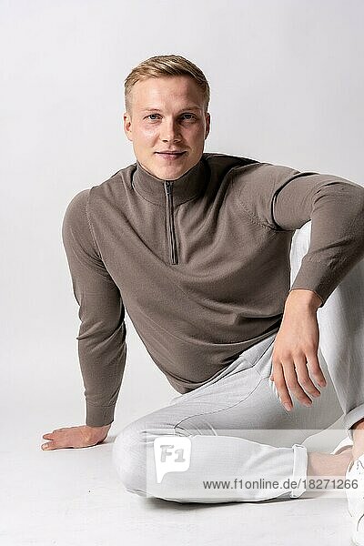 Blond caucasian model with brown sweater on a white background  staring at the camera smiling