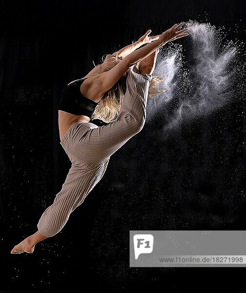 Junge Tänzerin  die einen Sprung auf einem schwarzen Hintergrund ausführt  Ballett  Einfrieren des Bildes mit Staub oder Mehl