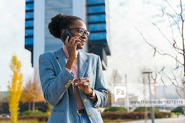 Portrait of black ethnic businesswoman wearing glasses in a business park  smiling talking on the phone