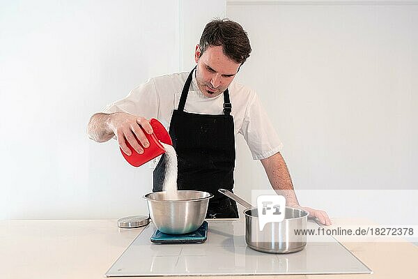 Hände eines Mannes  der zu Hause einen roten Samtkuchen backt  Schweizer Baiser mit Eischnee im Wasserbad zubereitet  Zucker hinzufügt  Arbeit zu Hause