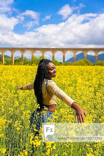 Lebensstil  die Natur in Freiheit genießen  Porträt eines schwarzen ethnischen Mädchens mit Zöpfen  Reisende  in einem Feld mit gelben Blumen