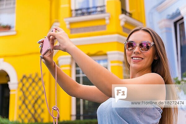 Junge attraktive blonde Frau  die ein Bild mit dem Telefon  hinter gelb und blau bunte Fassade