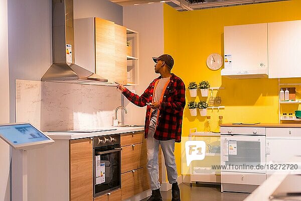Schwarzer ethnischer Mann  der in einem Möbelhaus einkauft und sich Küchenmöbel und Preise ansieht