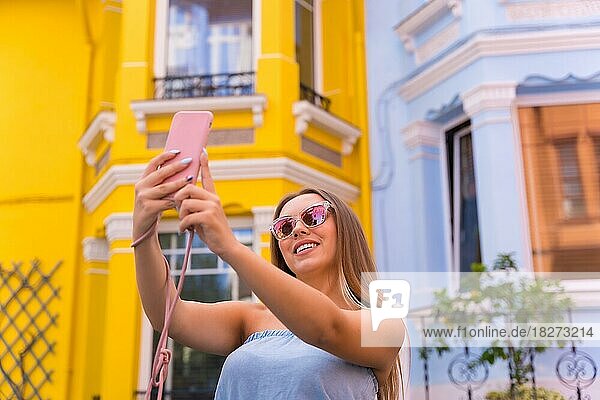 Porträt attraktive junge blonde Frau  die ein Selfie  hinter gelb und blau bunte Fassade