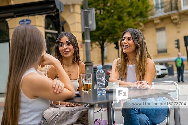 Portrait of young women friends having something one afternoon on a terrace of a cafeteria in autumn