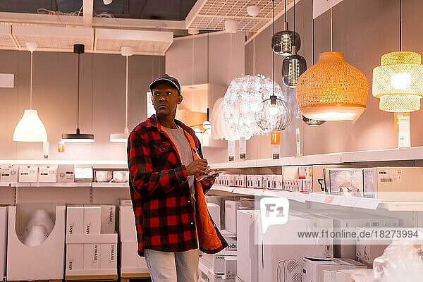 Black ethnic man shopping in a supermarket for lamps  with the shopping list