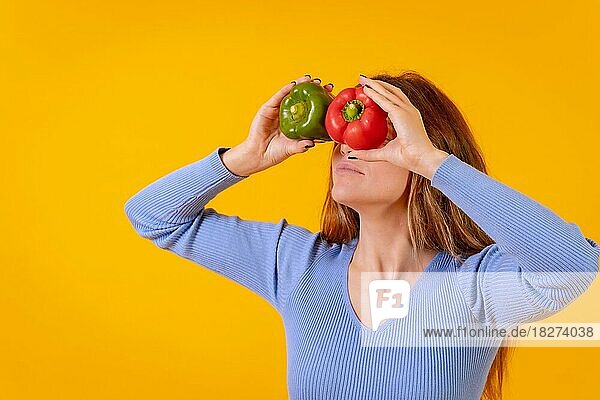 Vegetarische Frau mit einer Brille aus Paprika auf ihren Augen auf gelbem Hintergrund  die ihre Zunge herausstreckt
