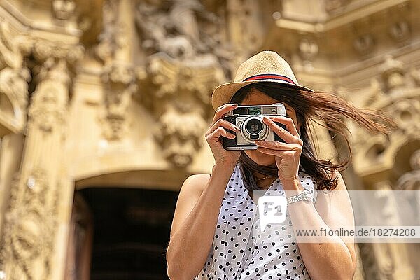 Eine Frau mit Hut  die die Stadt besichtigt und Fotos mit einer alten Kamera macht  die Sommerferien genießend  Konzept einer weiblichen Reisenden und Schöpferin digitaler Inhalte