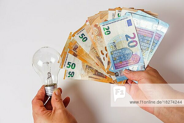 Woman holding banknotes in one hand and a light bulb in the other concept of light prices