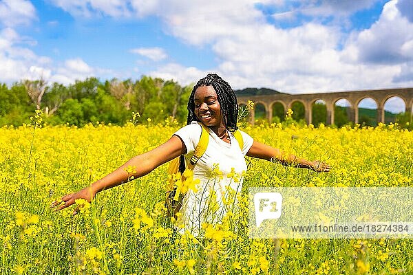 Ein schwarzes ethnisches Mädchen mit Zöpfen  eine Reisende  genießt die Freiheit in einem Feld mit gelben Blumen