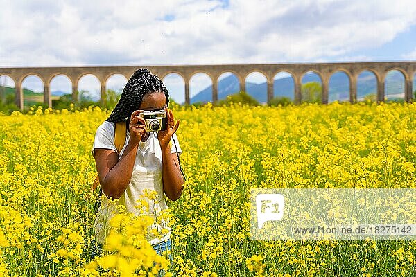 Fotografieren mit einer alten Kamera  ein schwarzes ethnisches Mädchen mit Zöpfen  eine Reisende  in einem Feld mit gelben Blumen