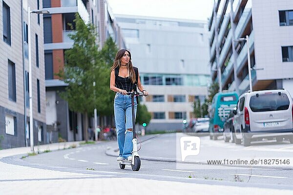 Eine junge brünette Frau  die sich in der Stadt mit einem Elektroroller auf dem Radweg bewegt