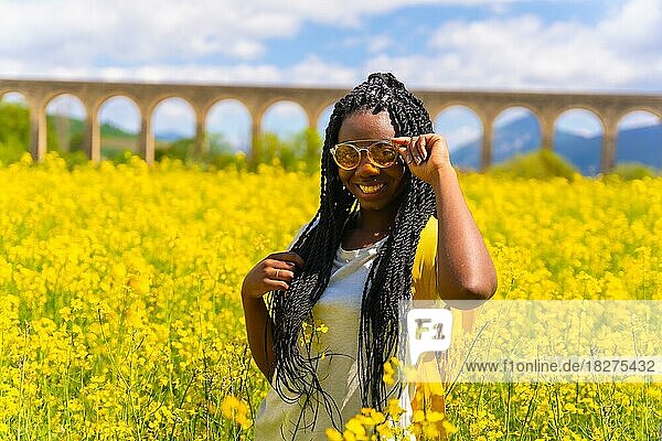 Porträt eines Mädchens schwarzer Hautfarbe mit Zöpfen und Sonnenbrille  Reisende  in einem Feld mit gelben Blumen